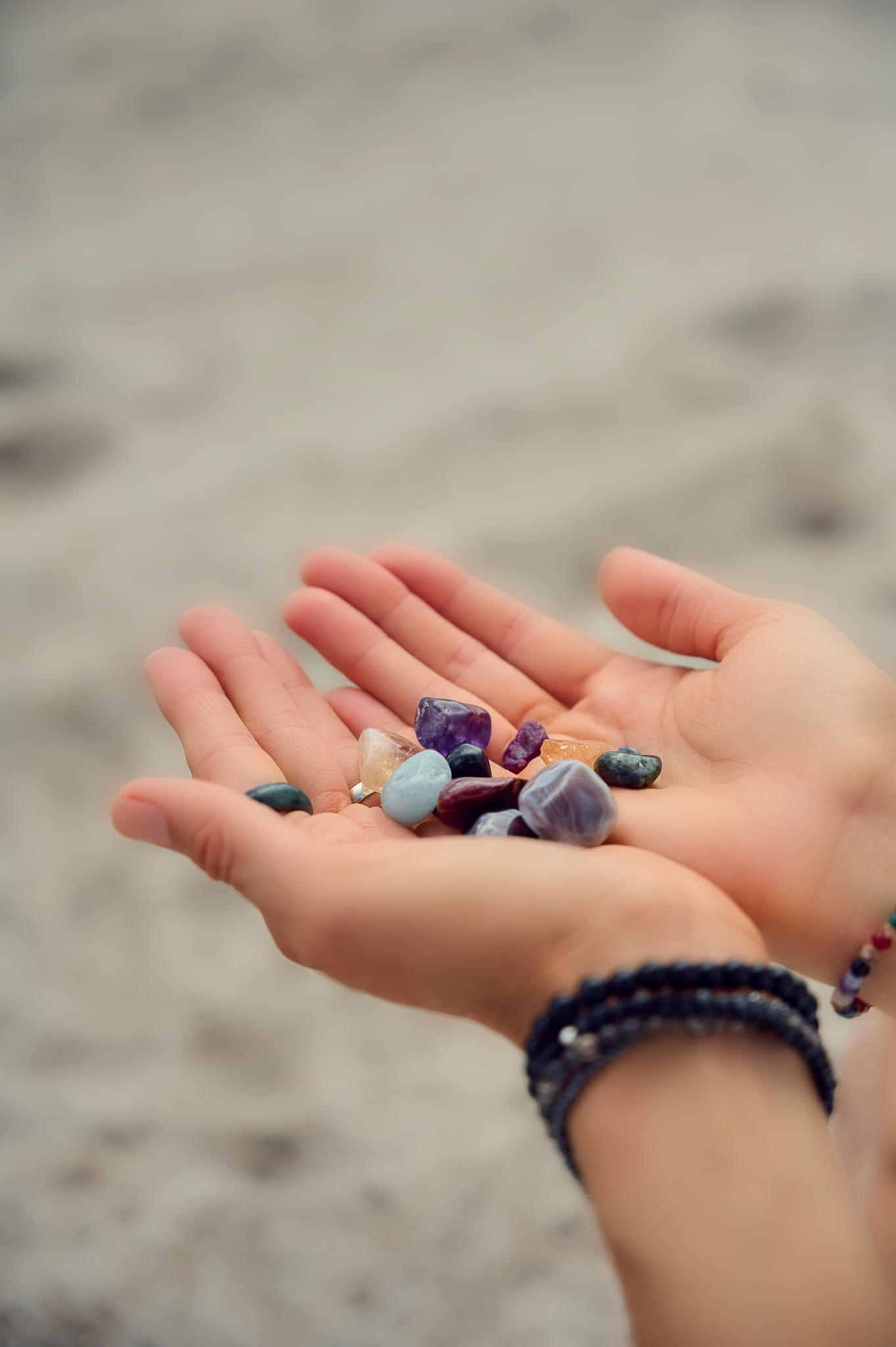 Open hands holding a collection of chosen crystals on the beach